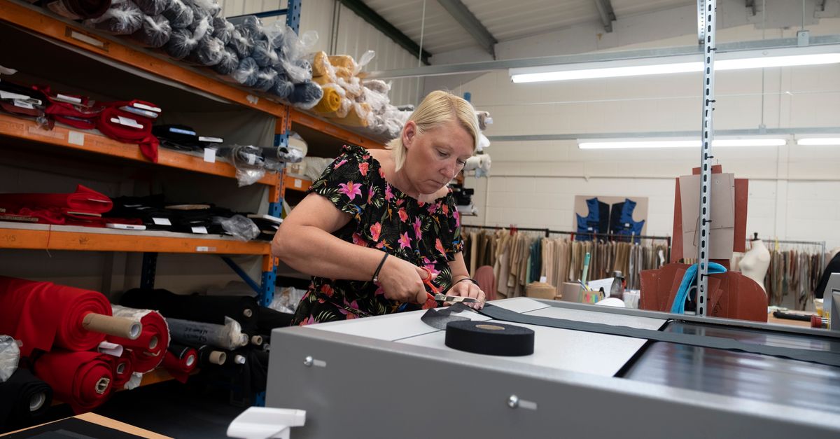 A female tailor cuts fabric in a well-organized factory workspace in England.