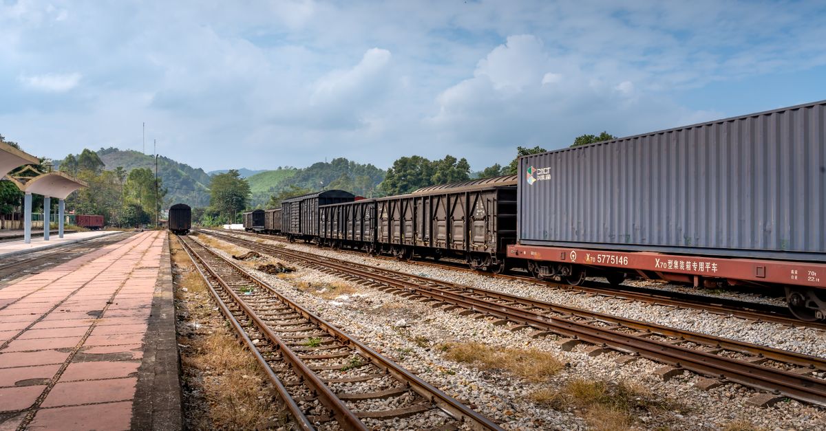 Cargo train with containers and tracks in a sunny outdoor railway setting.