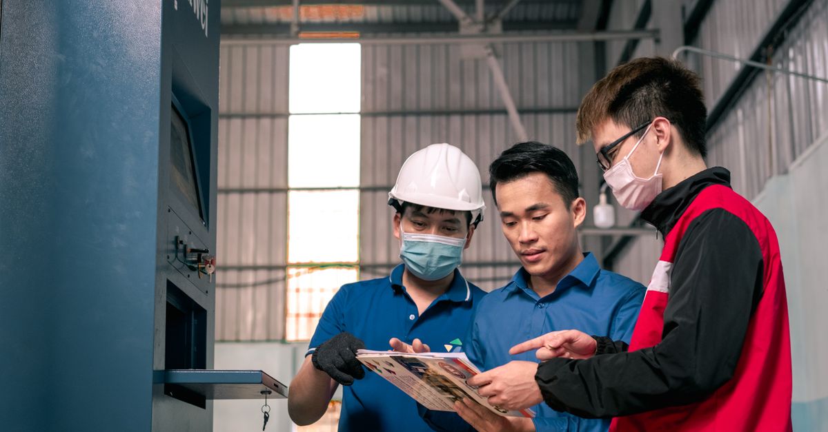 Workers in a warehouse reviewing blueprints, emphasizing teamwork and safety.