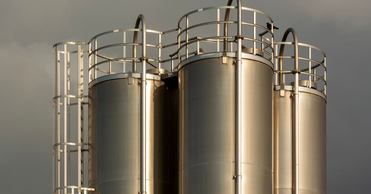 Close-up of industrial metal storage tanks against a backdrop of dark clouds, creating a dramatic industrial scene.