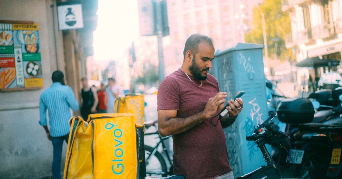 Delivery courier using his phone next to bicycle in a sunny urban street.