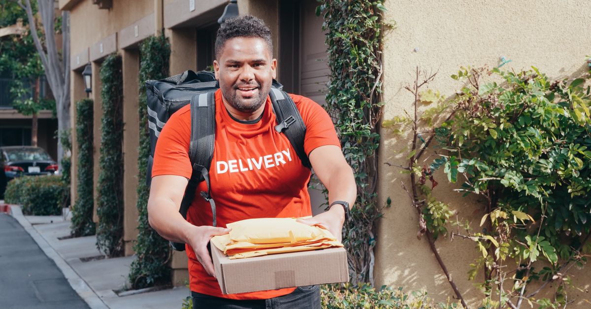 Friendly deliveryman in red delivering packages outdoors on a sunny day.