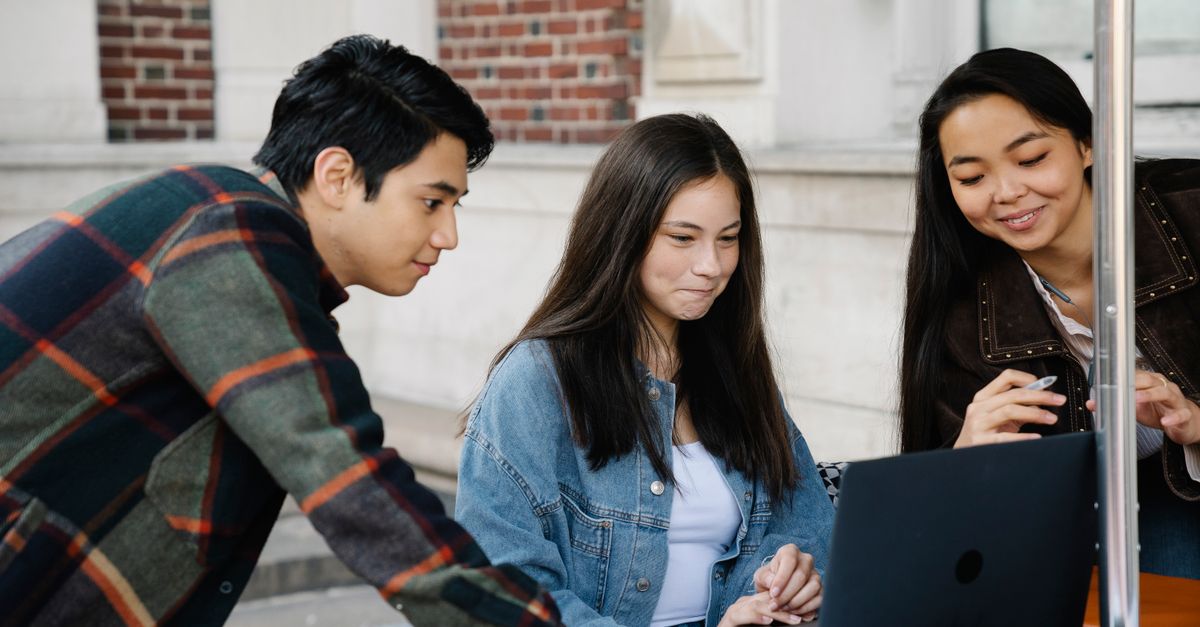 Diverse group of college students studying outdoors with a laptop, fostering collaboration.