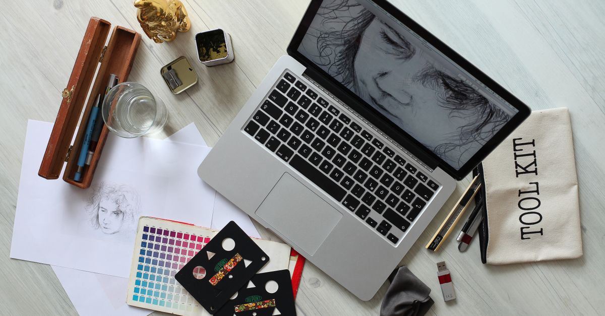 Top view of a creative workspace with a laptop, sketch supplies, and color palette.