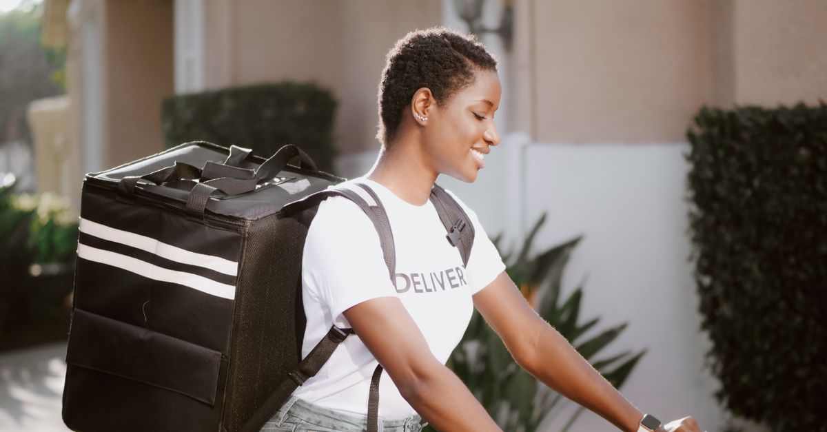 Smiling deliverywoman in uniform with delivery bag on the street during daytime.