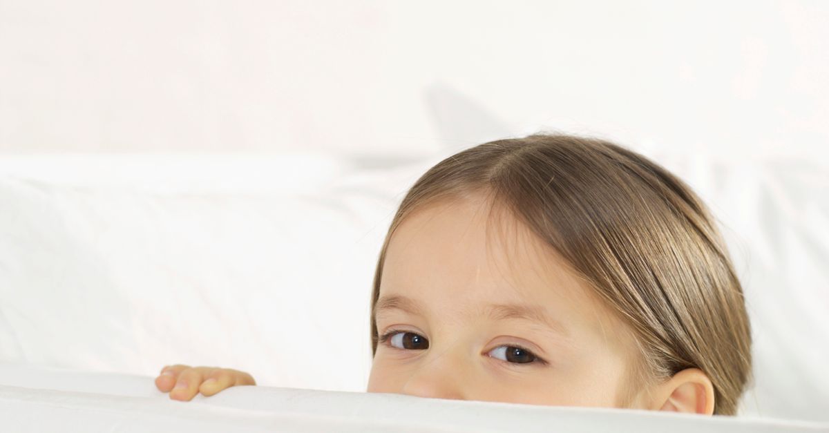 A cute child peeks over a white blanket, showcasing innocence and curiosity.