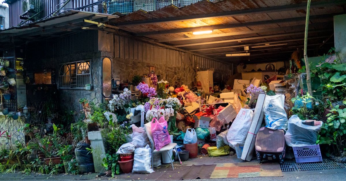 A garage filled with various household items, plants, and clutter overflowing onto the street.