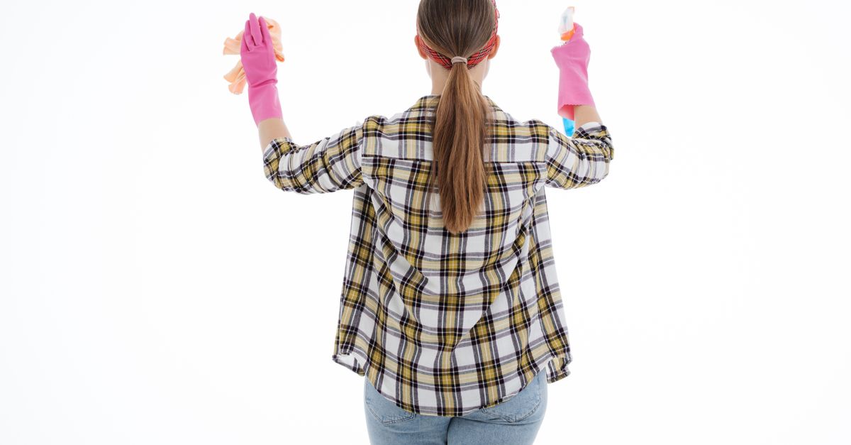 Back view of a woman in latex gloves cleaning with spray and cloth, indoor studio shot.