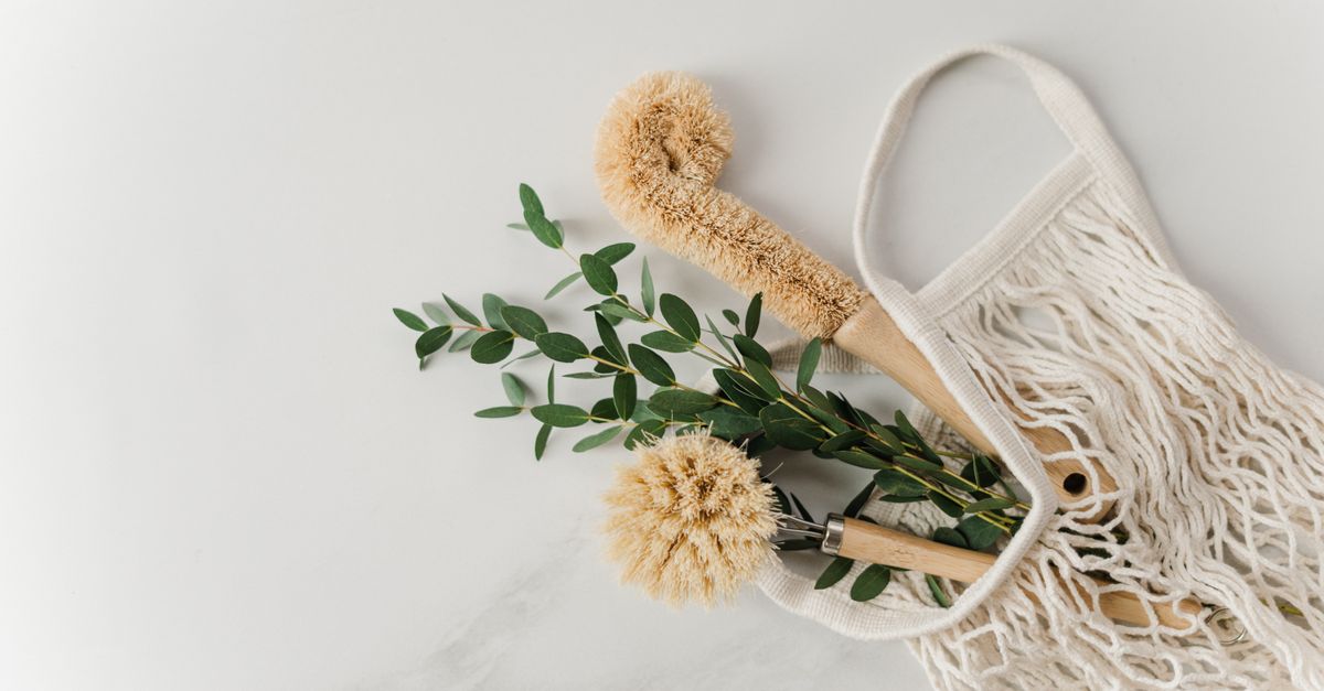 Eco-friendly cleaning brushes and eucalyptus branches in a reusable net bag on white surface.