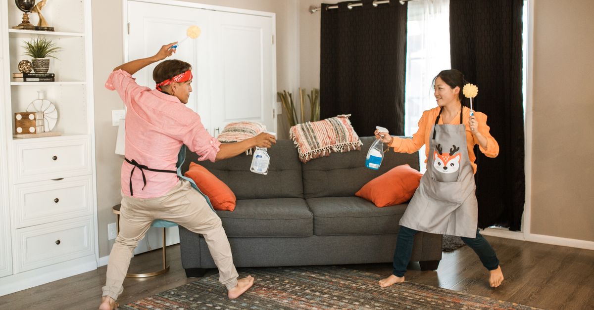 A joyful couple engages in a playful cleaning fight in their living room, showcasing light-hearted domestic life.