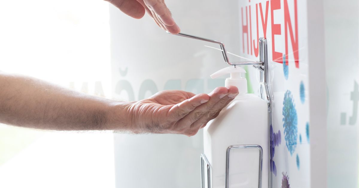 Close-up of hands using a liquid disinfectant dispenser in a clean environment emphasizing hygiene.