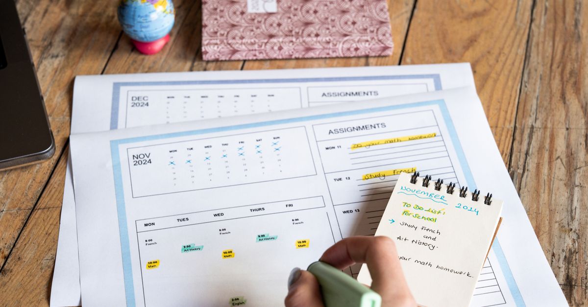 Person planning tasks with a calendar and notepad on a wooden table.