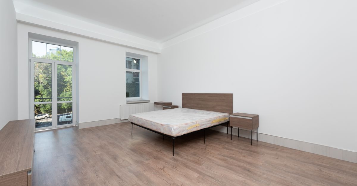 Spacious minimalist bedroom featuring wooden floors and large windows for natural light.