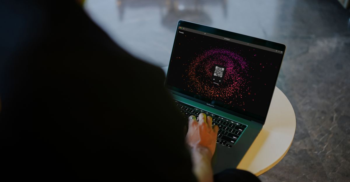 A person interacts with a colorful QR code display on a laptop in a modern indoor setting.