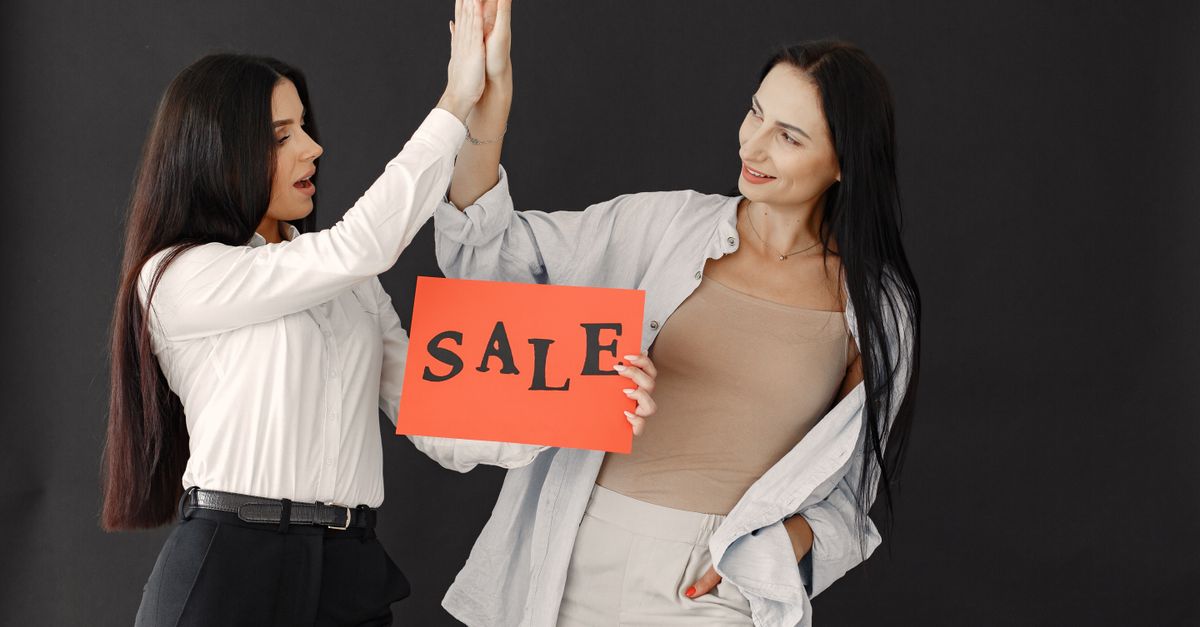 Two women celebrating a sale with a high five, holding a 'SALE' sign.
