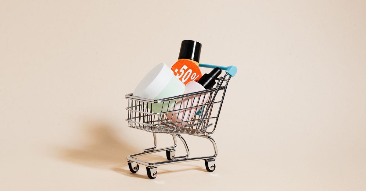 Mini shopping cart with cosmetics and a 50% discount sign on a neutral background.