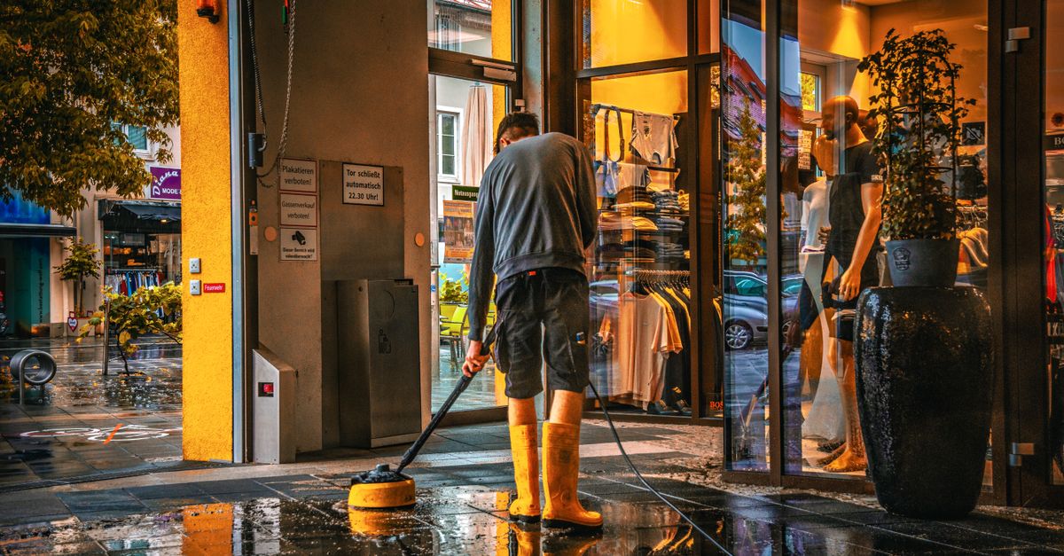 A man cleans the entrance of a store during a rainy day, reflecting urban life.
