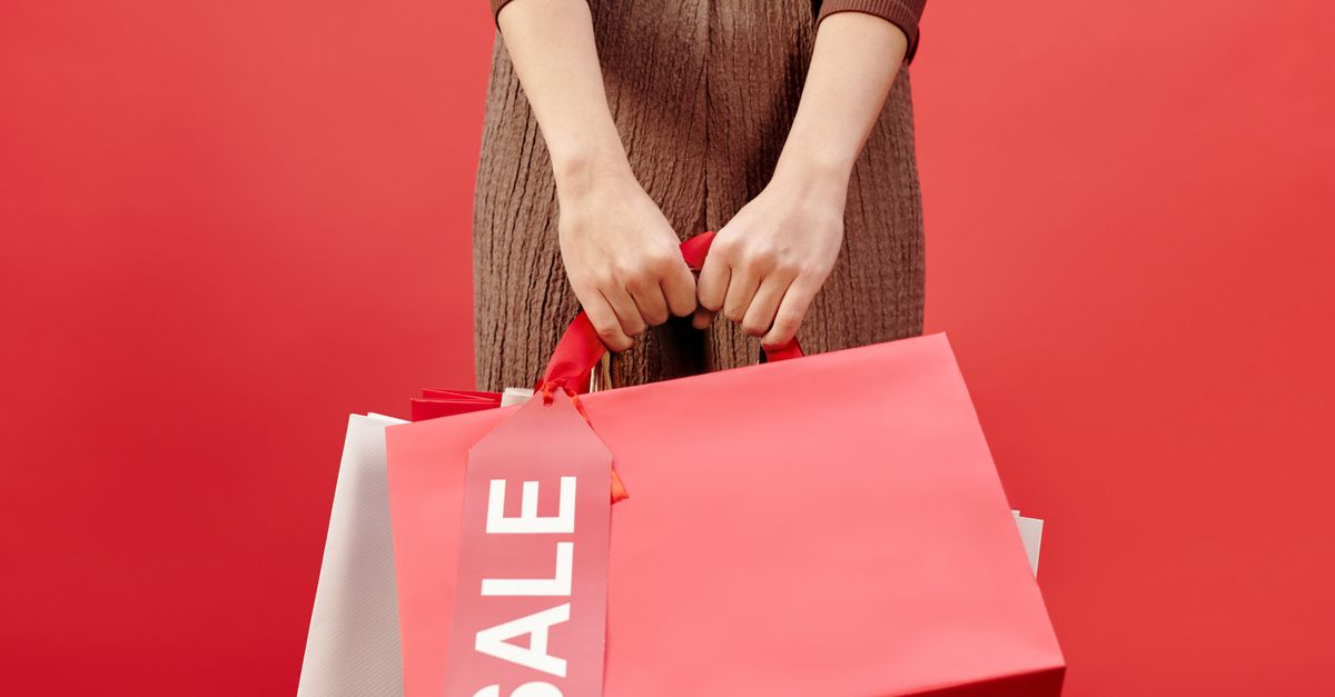 Close-up of a person holding shopping bags with a sale tag on a red background.