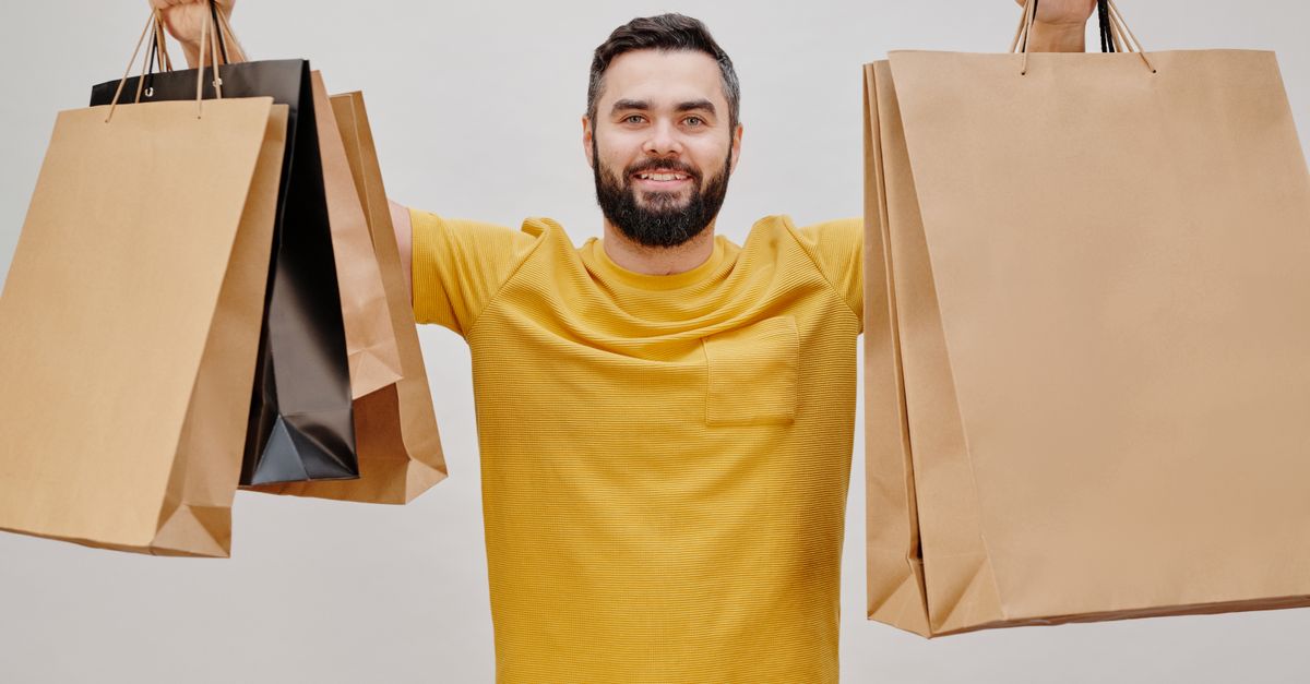 Happy man in yellow shirt holding multiple shopping bags, expressing joy of shopping.
