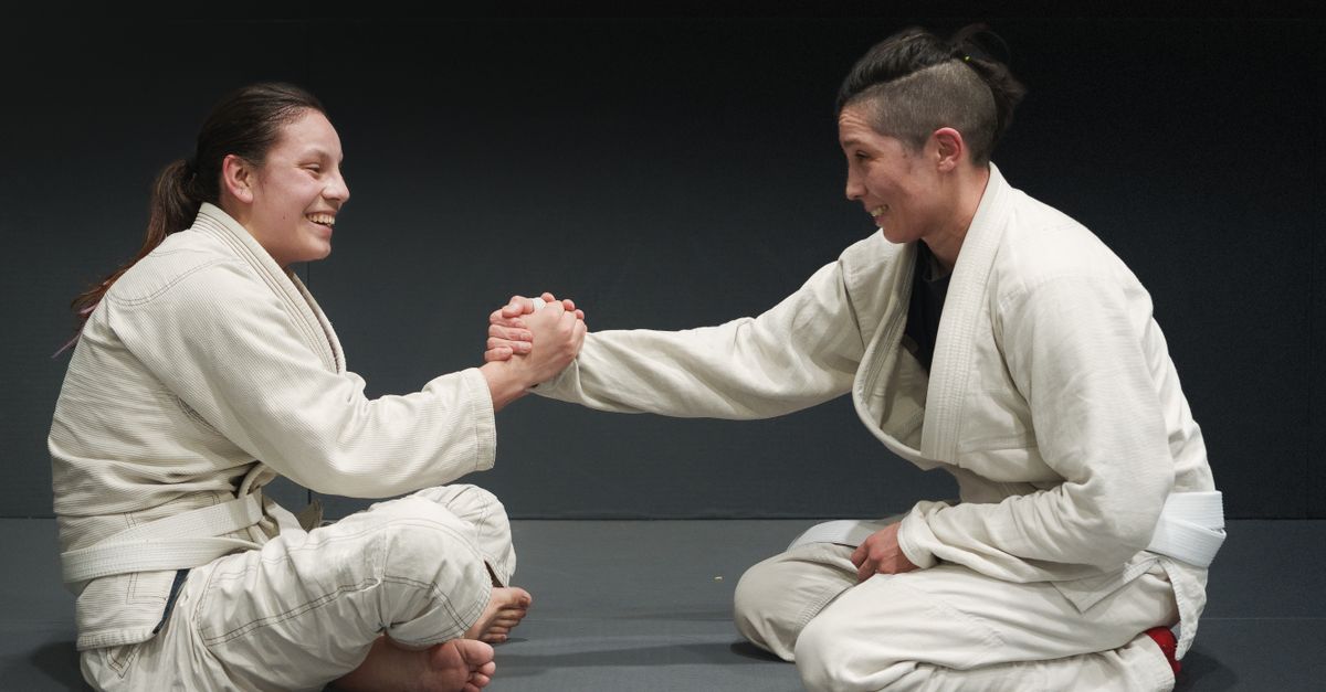 Two women in a jiu-jitsu dojo share a friendly handshake after training in Buenos Aires.