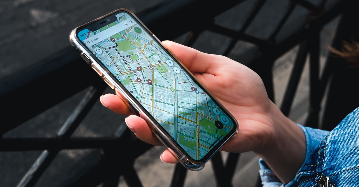 An outdoor close-up of a hand holding a smartphone displaying a map application.