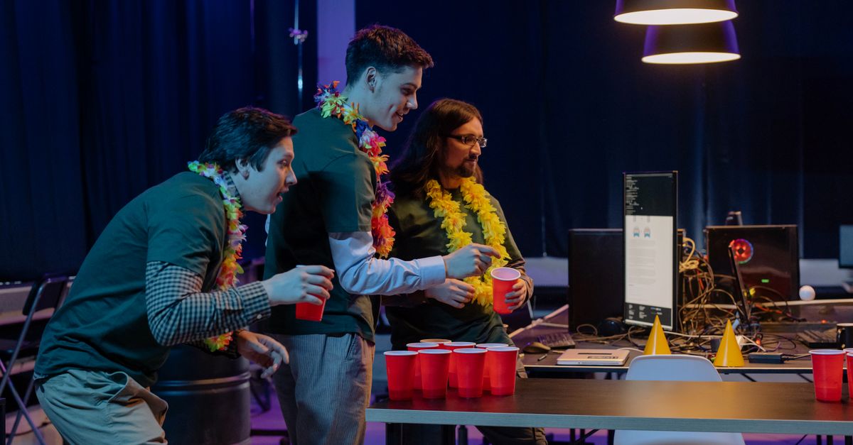 Group of male colleagues enjoying a fun beer pong game during an office party night.