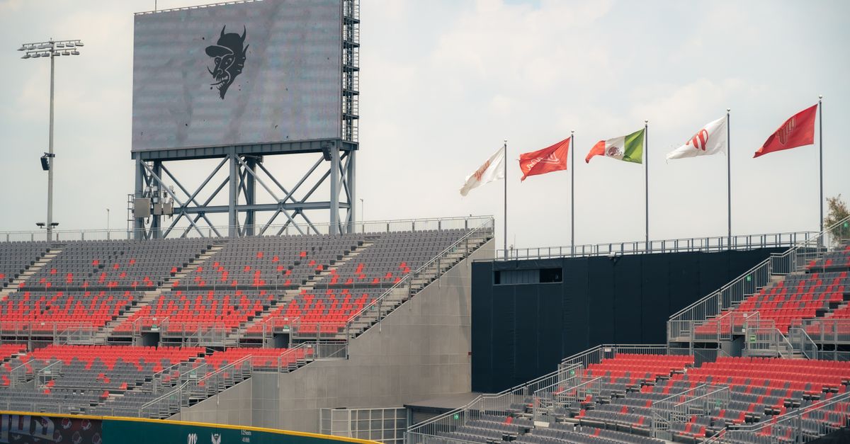 A modern stadium featuring red and gray seating and international flags, under a cloudy sky.