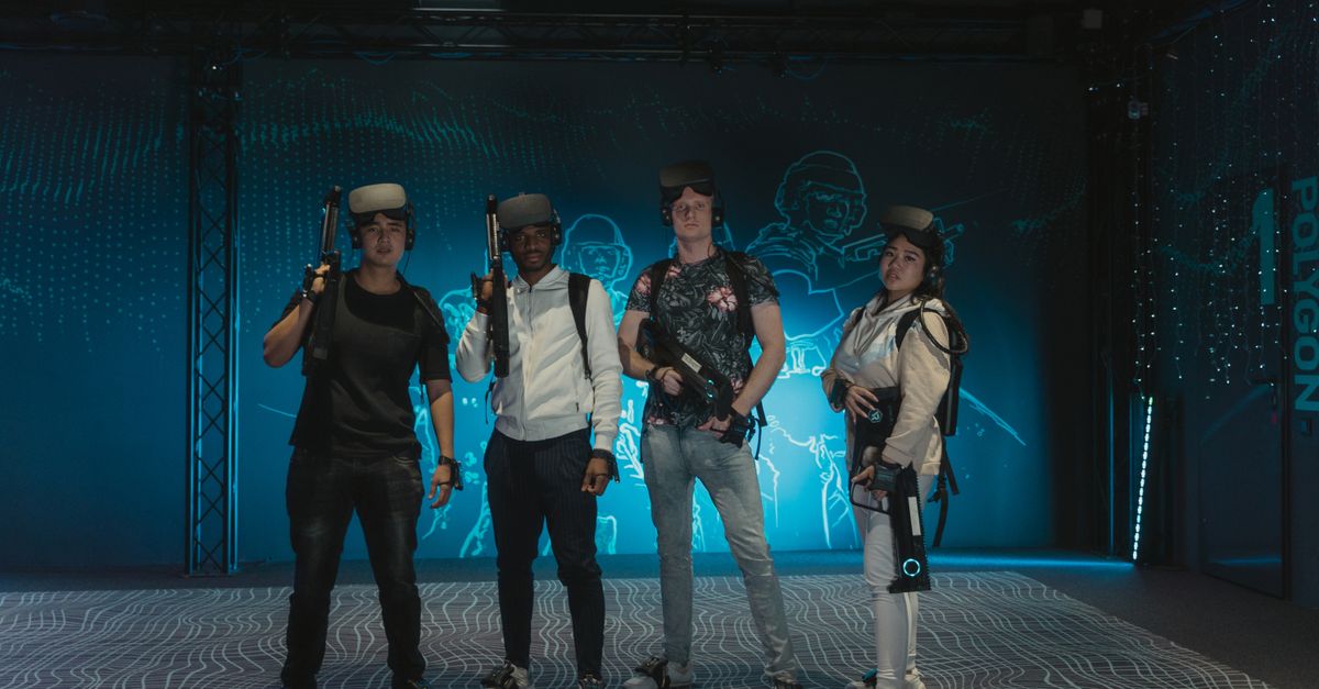 A diverse group of friends playing with VR headsets and guns in a gaming arena.