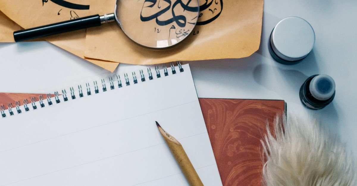 Artistic flat lay of calligraphy tools, notepad, and magnifying glass for creative inspiration.