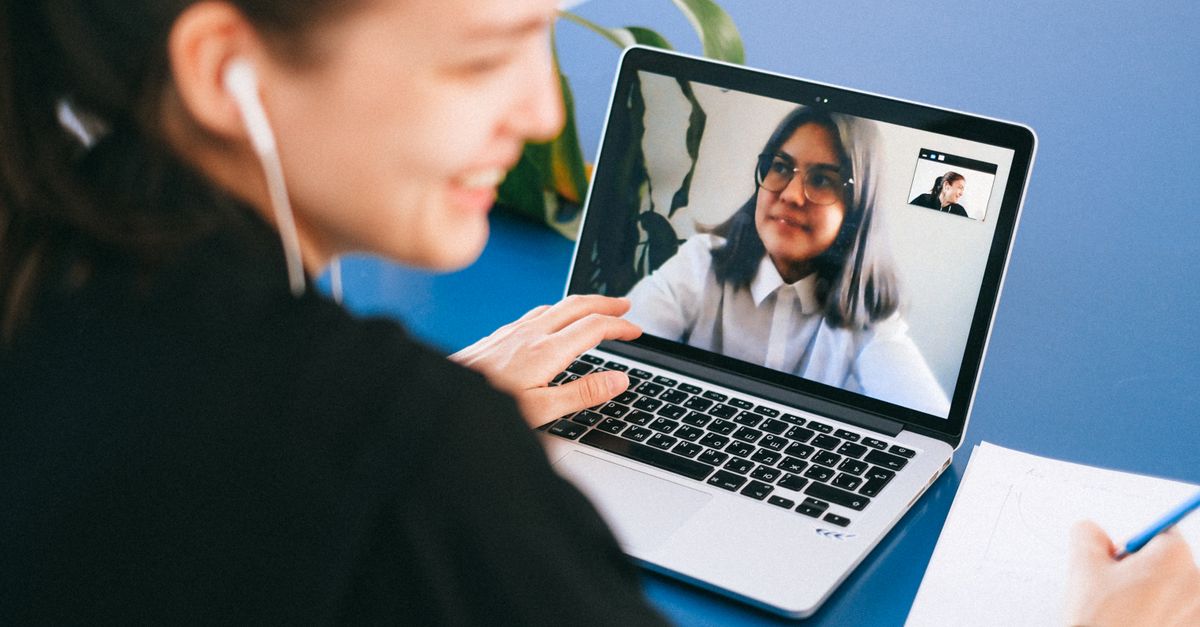 Woman having a video conference on a laptop, smiling and taking notes.