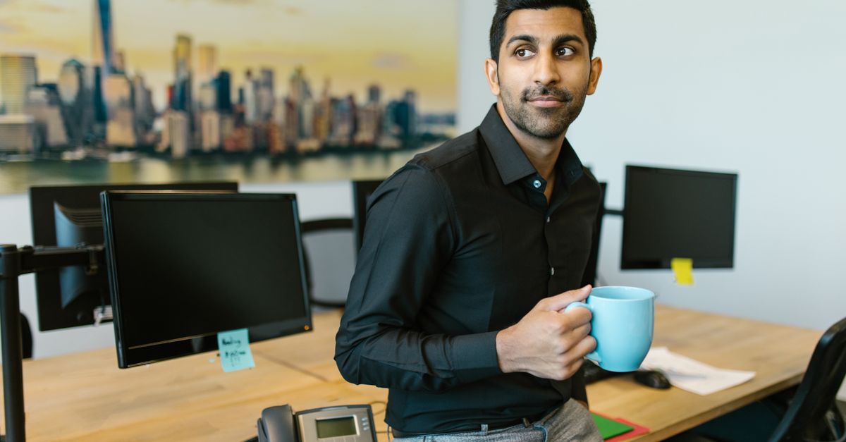 Confident Indian businessman enjoying a coffee break in a modern office space.