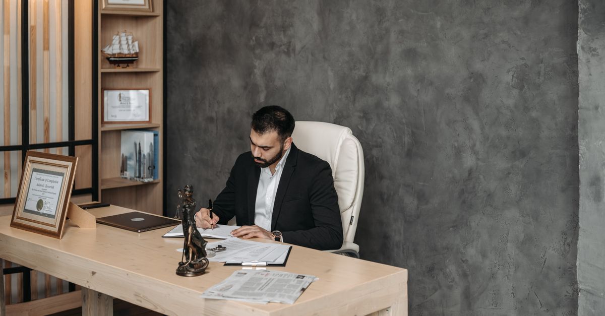 Businessman in a suit writing at a desk in a modern office setting.