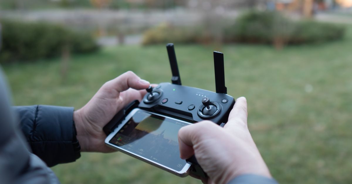 Close-up of hands operating a drone controller with a smartphone attached in an outdoor setting.