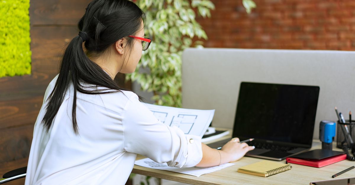 Woman working diligently at a laptop in a modern office environment.