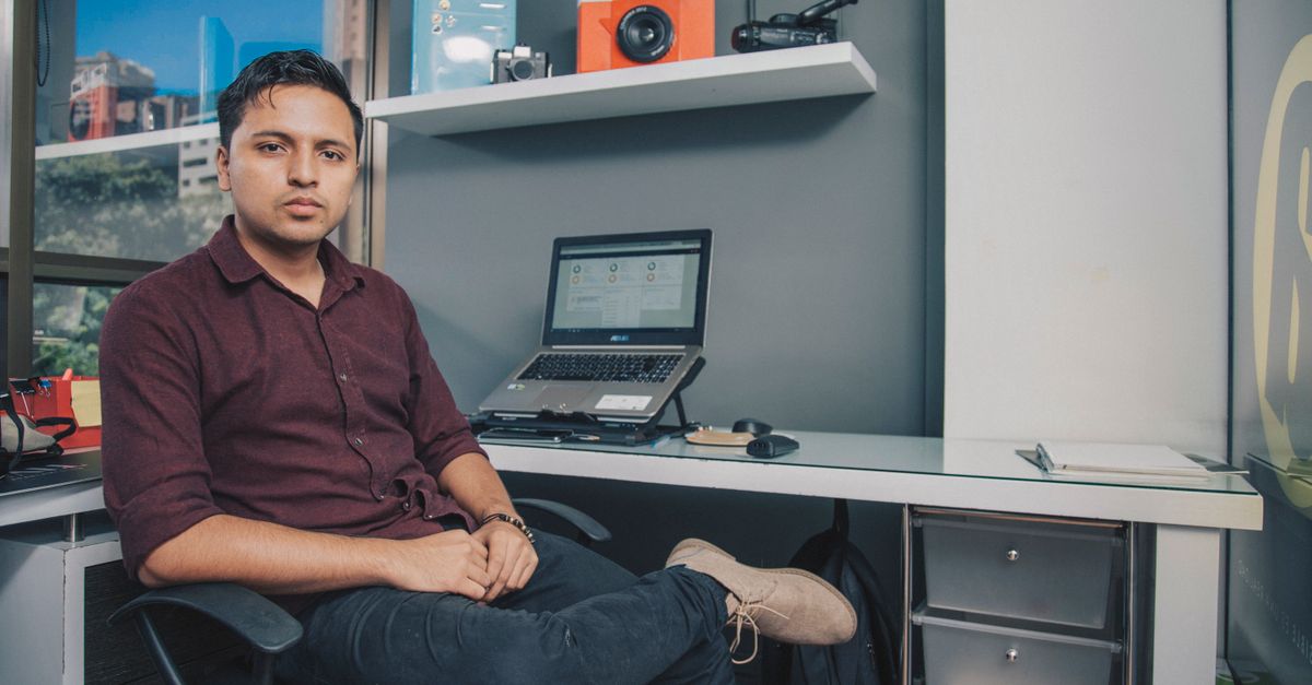 Young entrepreneur sitting at office desk with laptop and gadgets, Antioquia, Colombia.