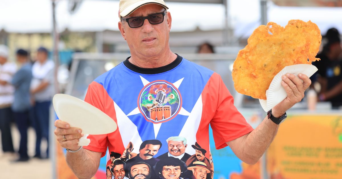 Man enjoying a large crispy snack outdoors, wearing a colorful printed shirt and sunglasses.