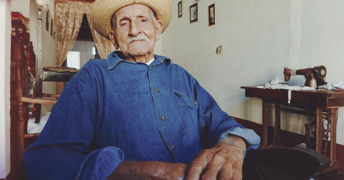 Elderly man in denim and straw hat sitting indoors, portraying the essence of retirement and vintage lifestyle.