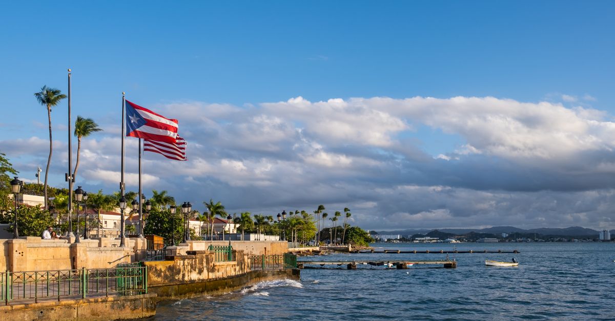 A picturesque view of the Puerto Rican waterfront with a flag waving against a backdrop of the sea and cityscape.