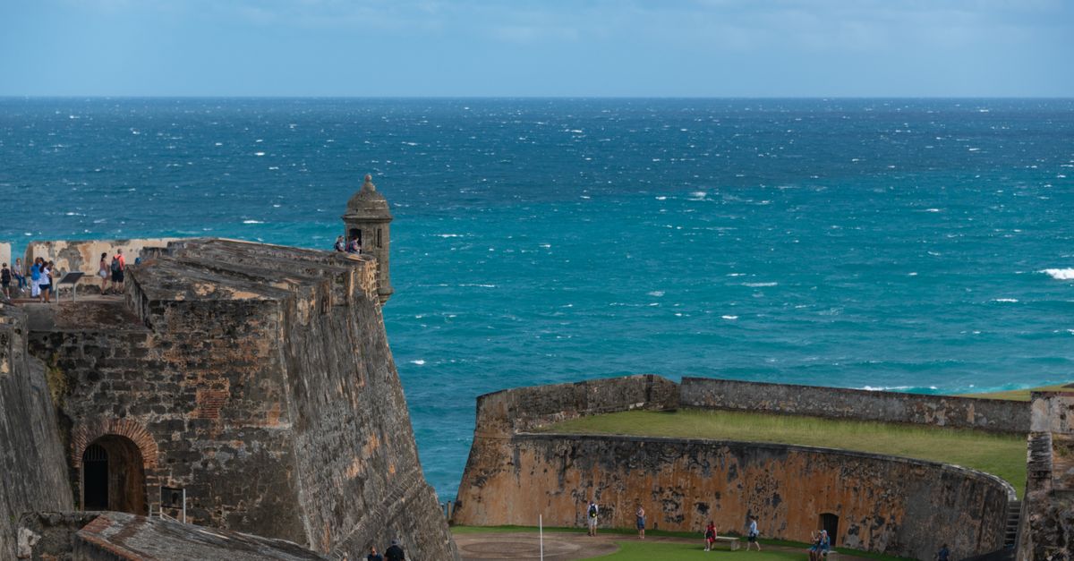 A view of the historic El Morro Fort in Puerto Rico with a backdrop of the ocean and people exploring.