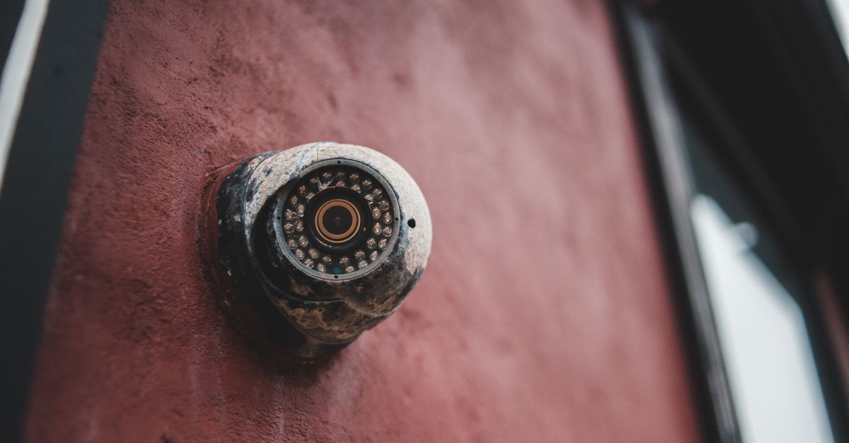 From below of aged surveillance camera with rough surface on uneven wall of house in daytime