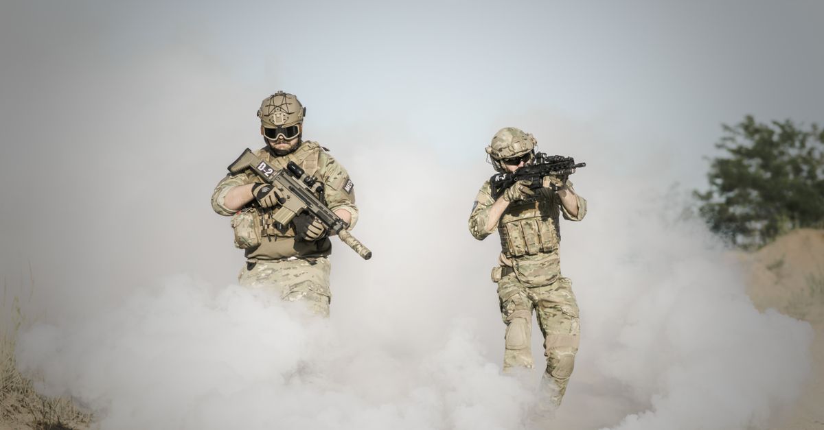 Two soldiers in full gear advancing through smoke during a military operation.