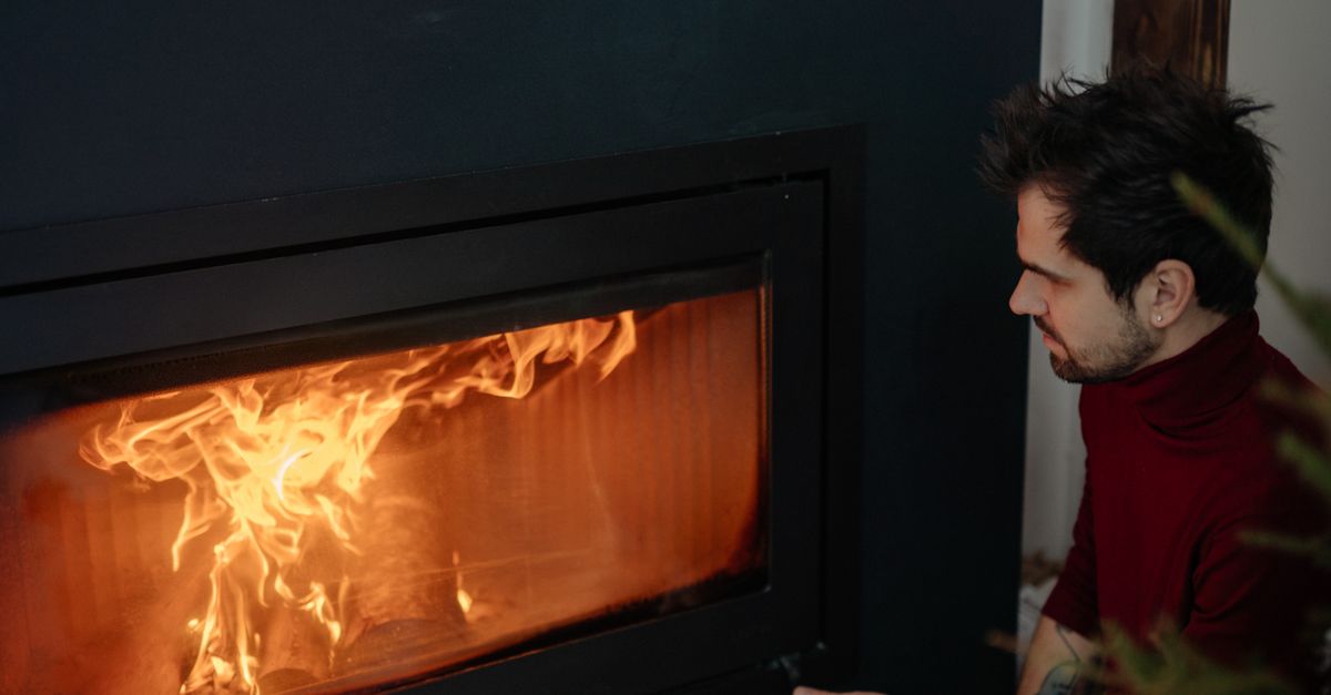 Man in cozy red sweater enjoying warmth from modern fireplace indoors.