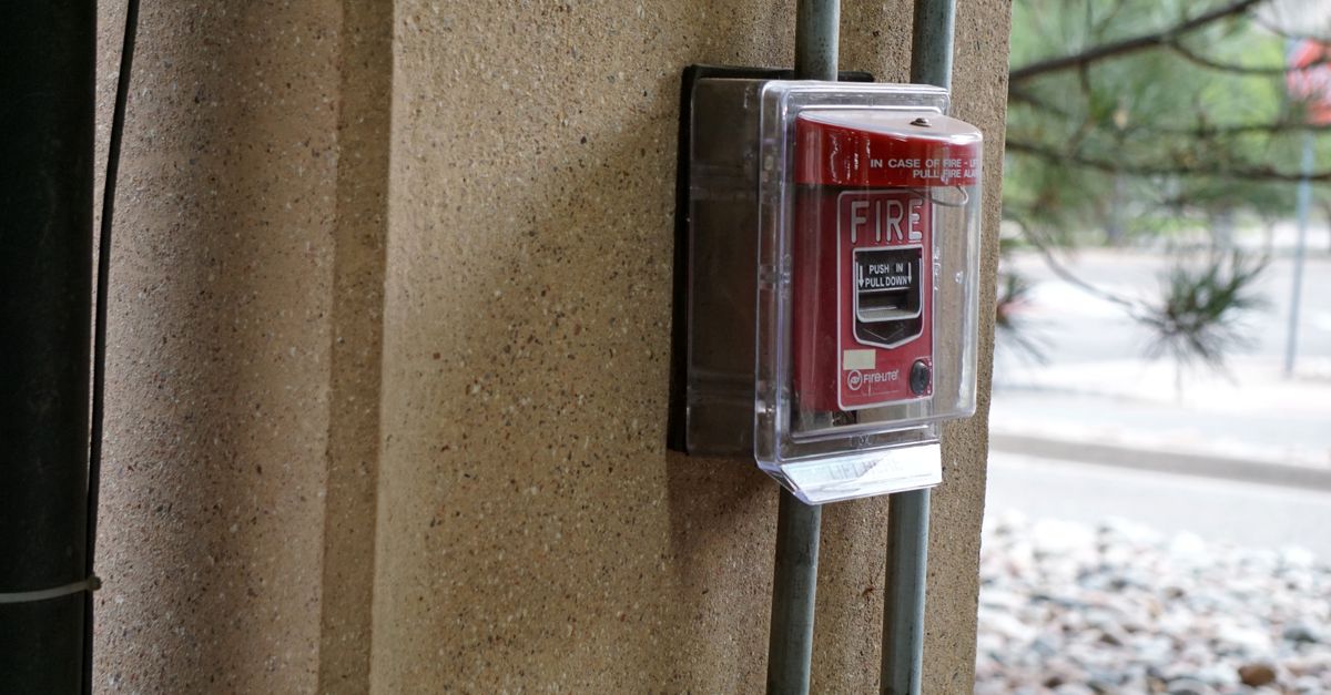 Close-up view of a red fire alarm mounted on a textured outdoor wall, showcasing safety equipment.