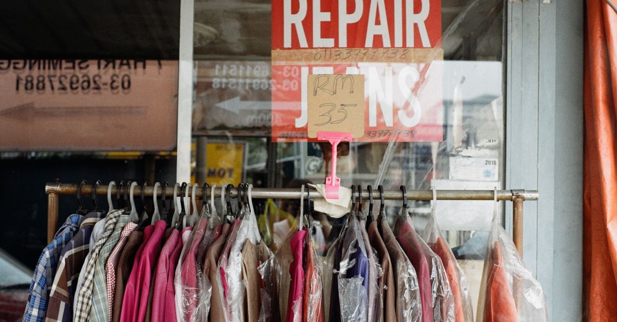 A clothing rack with various garments outside a tailor shop with a repair sign.
