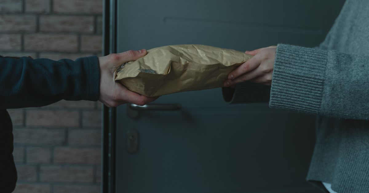 Close-up of hands exchanging a package at a doorway, symbolizing home delivery service.