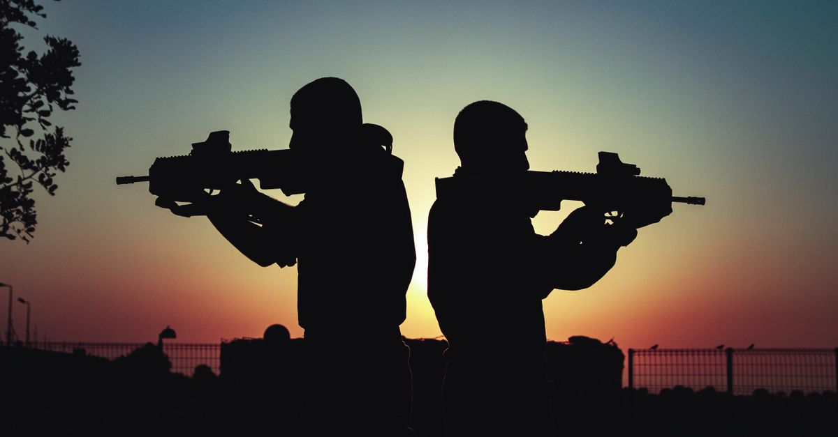 Silhouette of two soldiers with rifles against a vivid sunset sky, creating a dramatic scene.