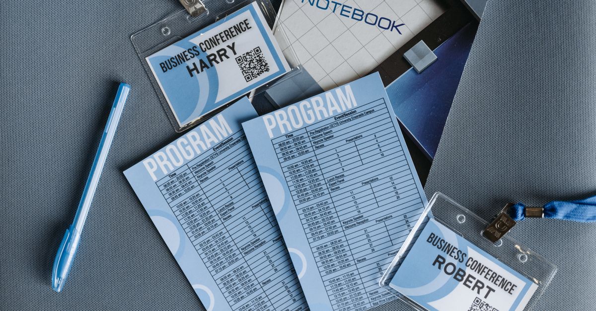 Flat lay of business conference materials including name tags, program, notebook, and pen.