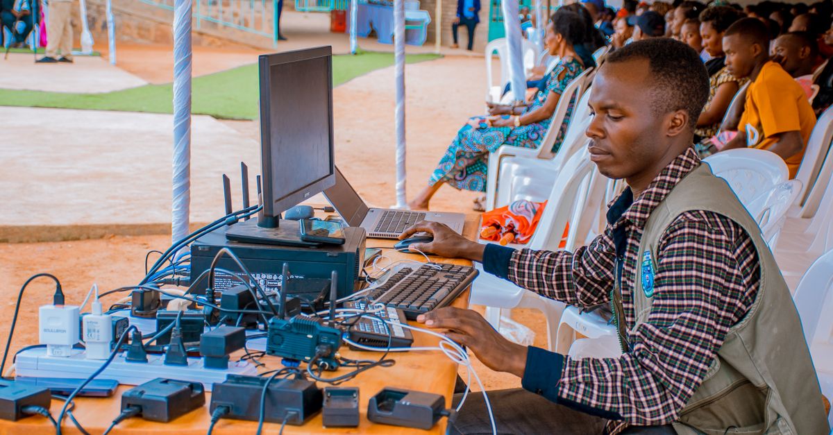 Technician managing electrical and computer setup at an outdoor event with attentive audience.