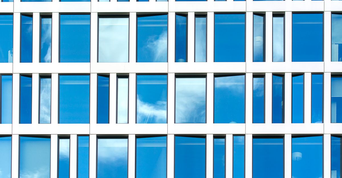 Elegant glass facade with geometric pattern reflecting sky clouds in Den Haag, Netherlands.