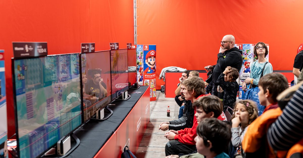 A lively group enjoys gaming at a Nintendo event in Zagreb, featuring multiple screens and vibrant atmosphere.